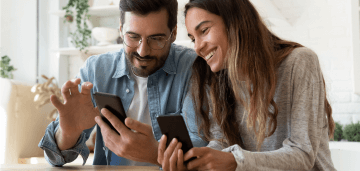 Happy couple sitting next to each other holding their smartphones