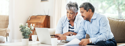Senior couple sitting together in their living room with a laptop and papers