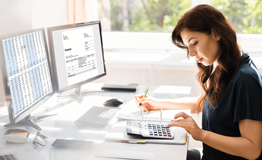 Woman sitting at desk with two computer monitors and a calculator