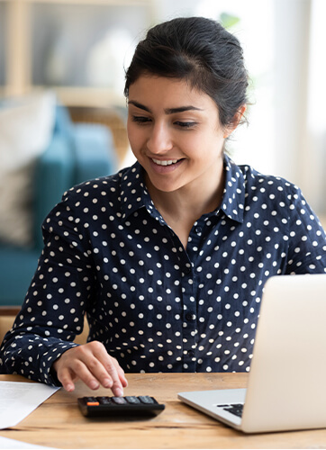 Woman with blue dress shirt smiling while using a calculator and computer