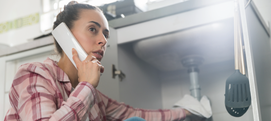Woman on the phone while fixing her sink of a possible leak