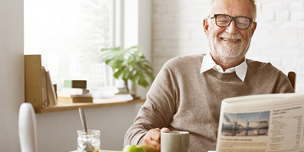 A man holding a mug, reading the paper, smiling