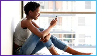 women sitting at window holding cell phone.